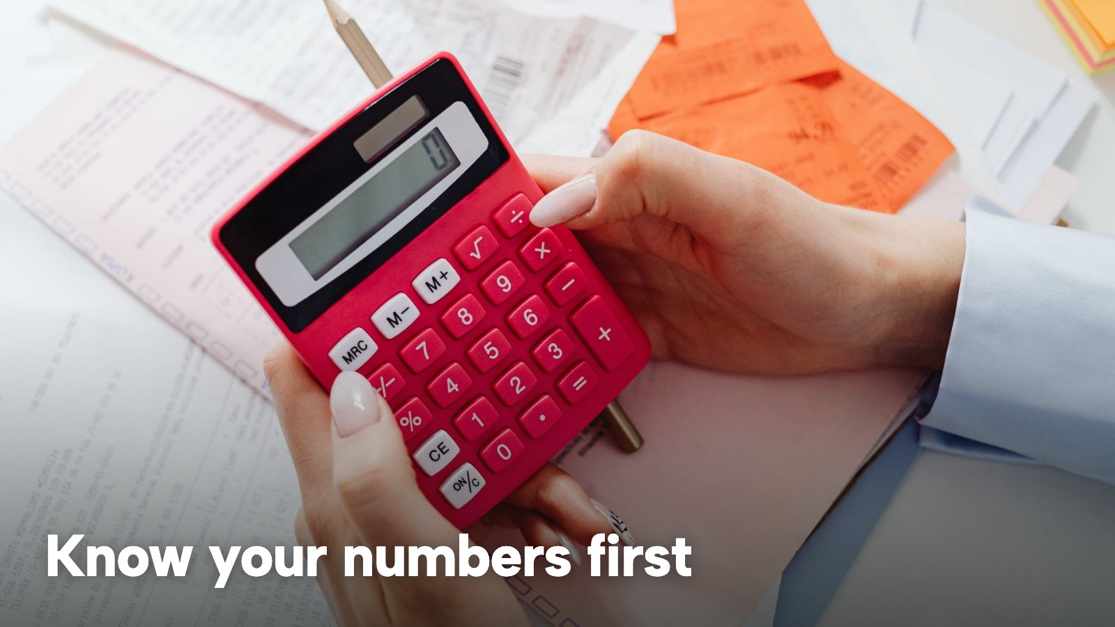 Hands hold a red calculator over a table of receipts and paperwork. The image carries the words "Know your numbers first".