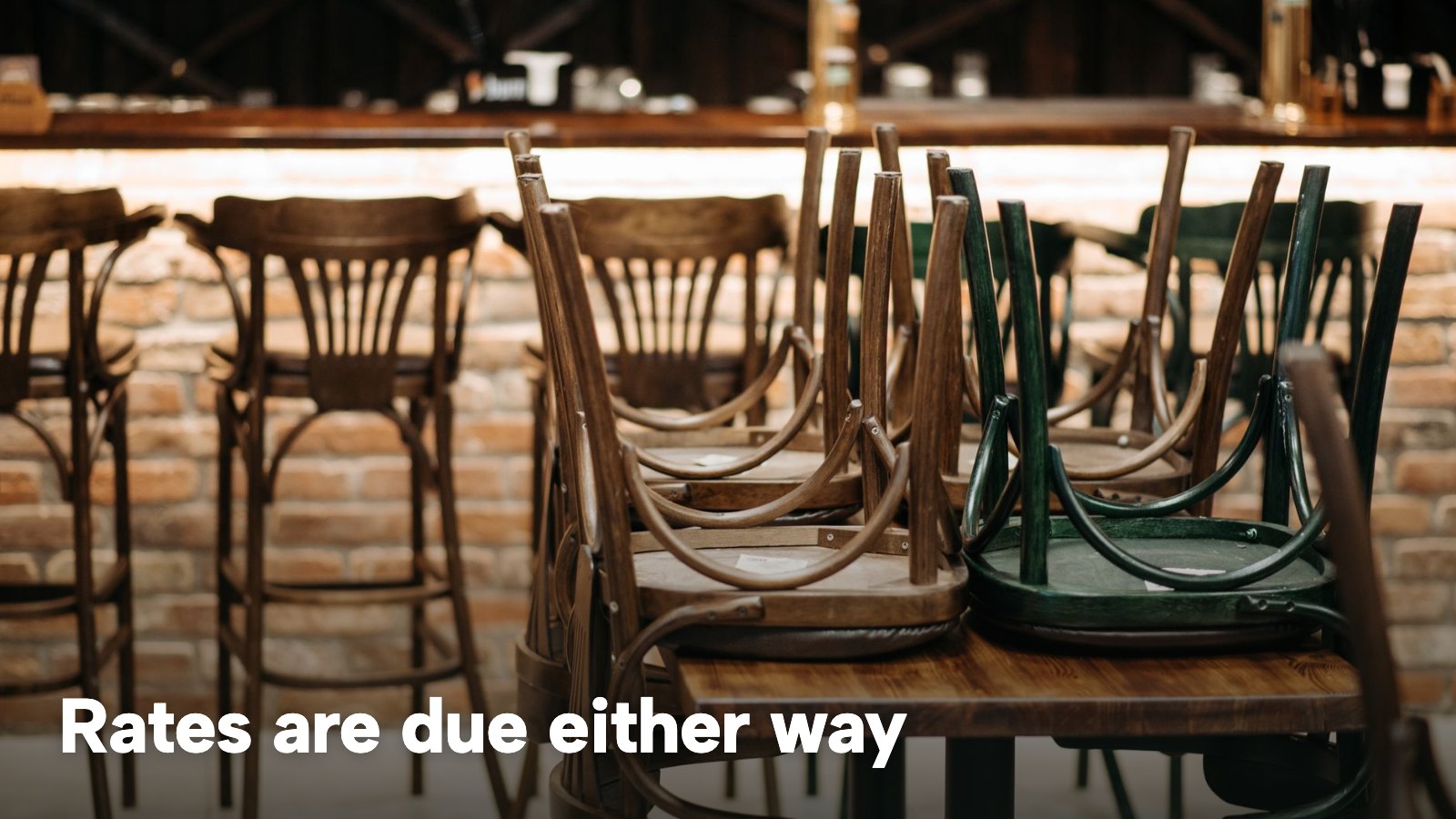 Wooden chairs stacked upside down on tables in an empty restaurant before opening. The image carries the words "Rates are due either way".