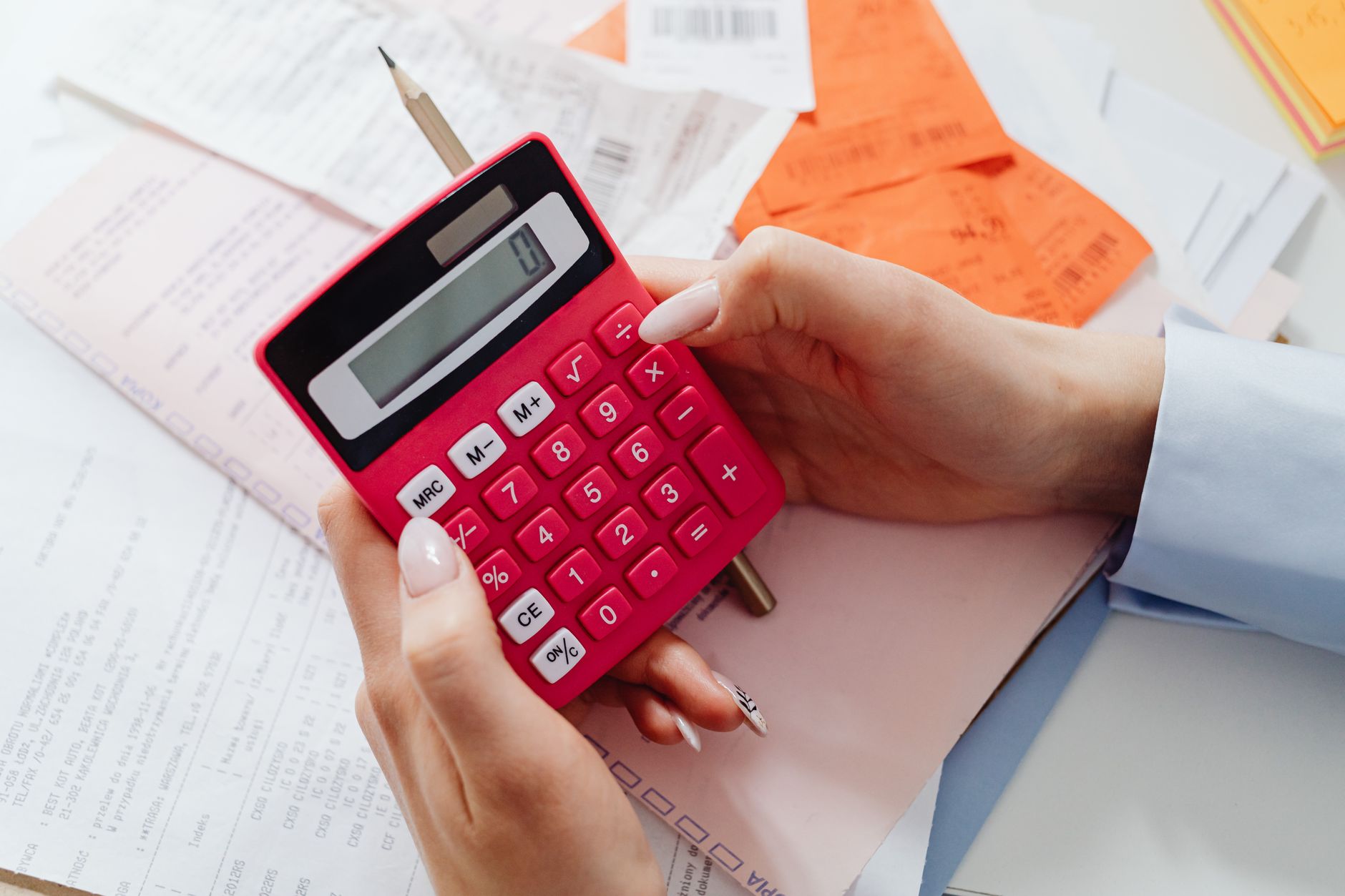 Hands hold a red calculator over a table of receipts and paperwork.