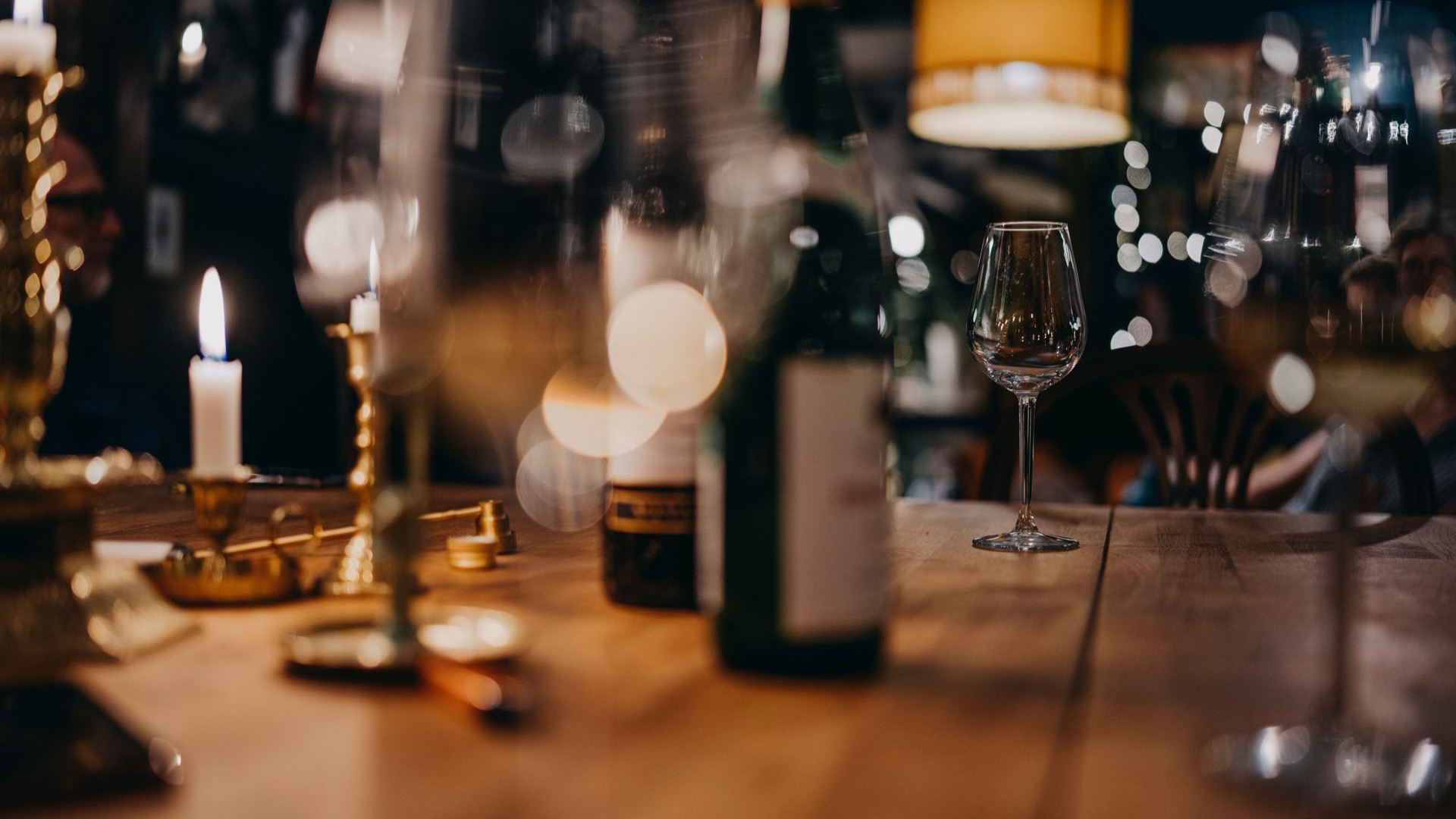 Wine glasses and candles on a wooden table in a dim bar.