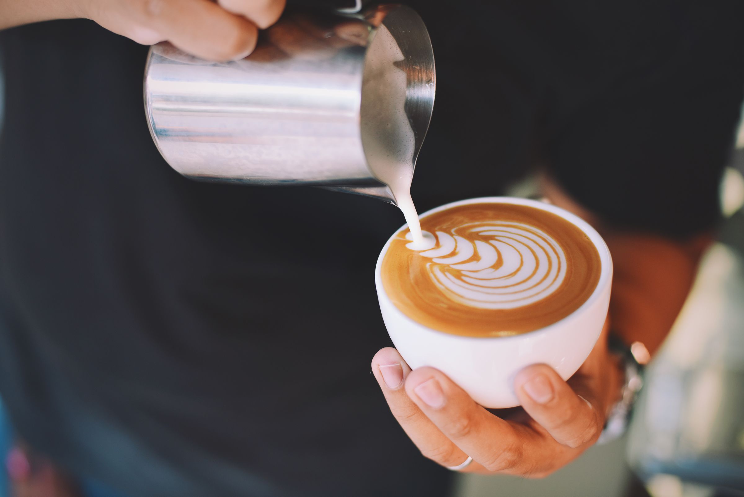 A barista pouring latte art into a cup.