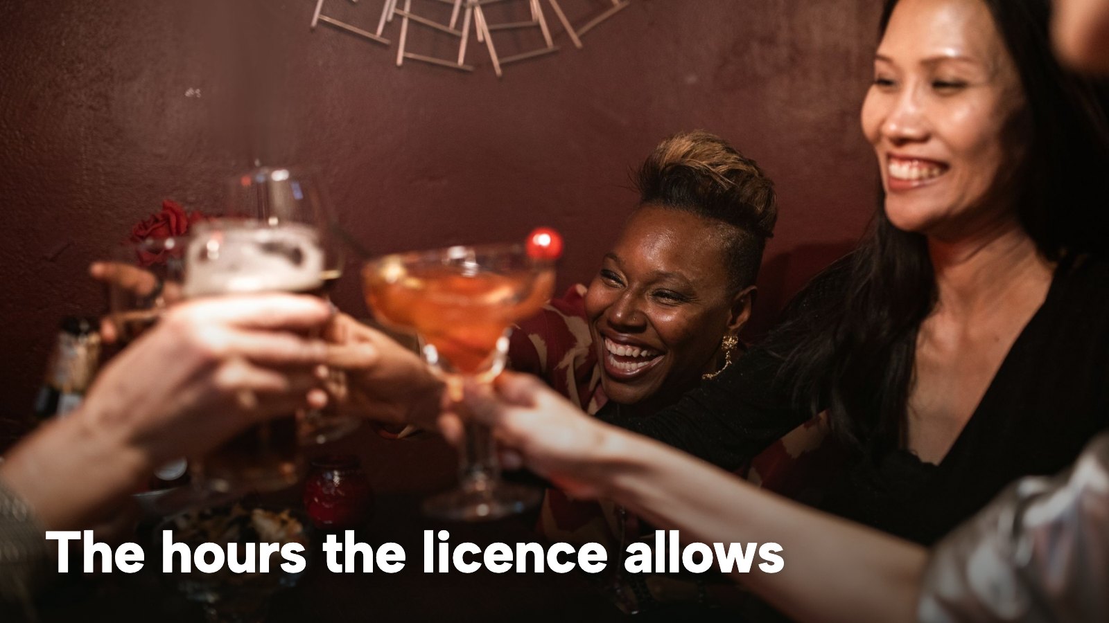 A group of friends toasting with drinks in a bar. The image carries the words "The hours the licence allows".