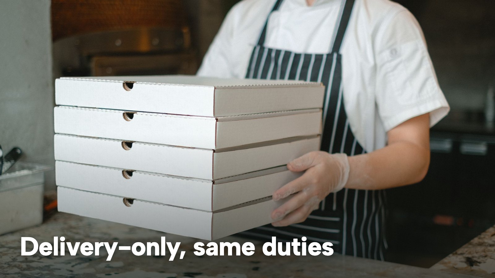 A delivery worker carries a tall stack of pizza boxes through a restaurant kitchen. The image carries the words "Delivery-only, same duties".