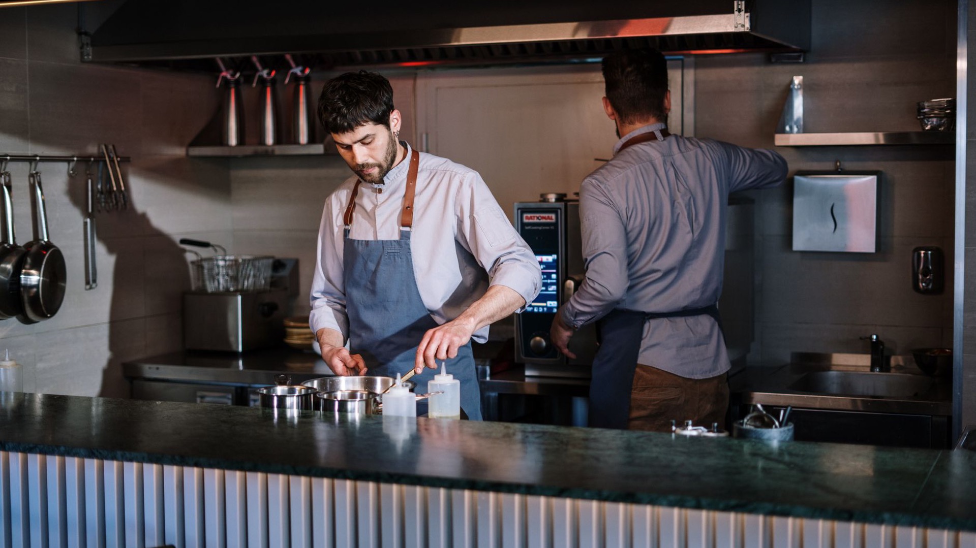 Two chefs working at an open steel kitchen line.