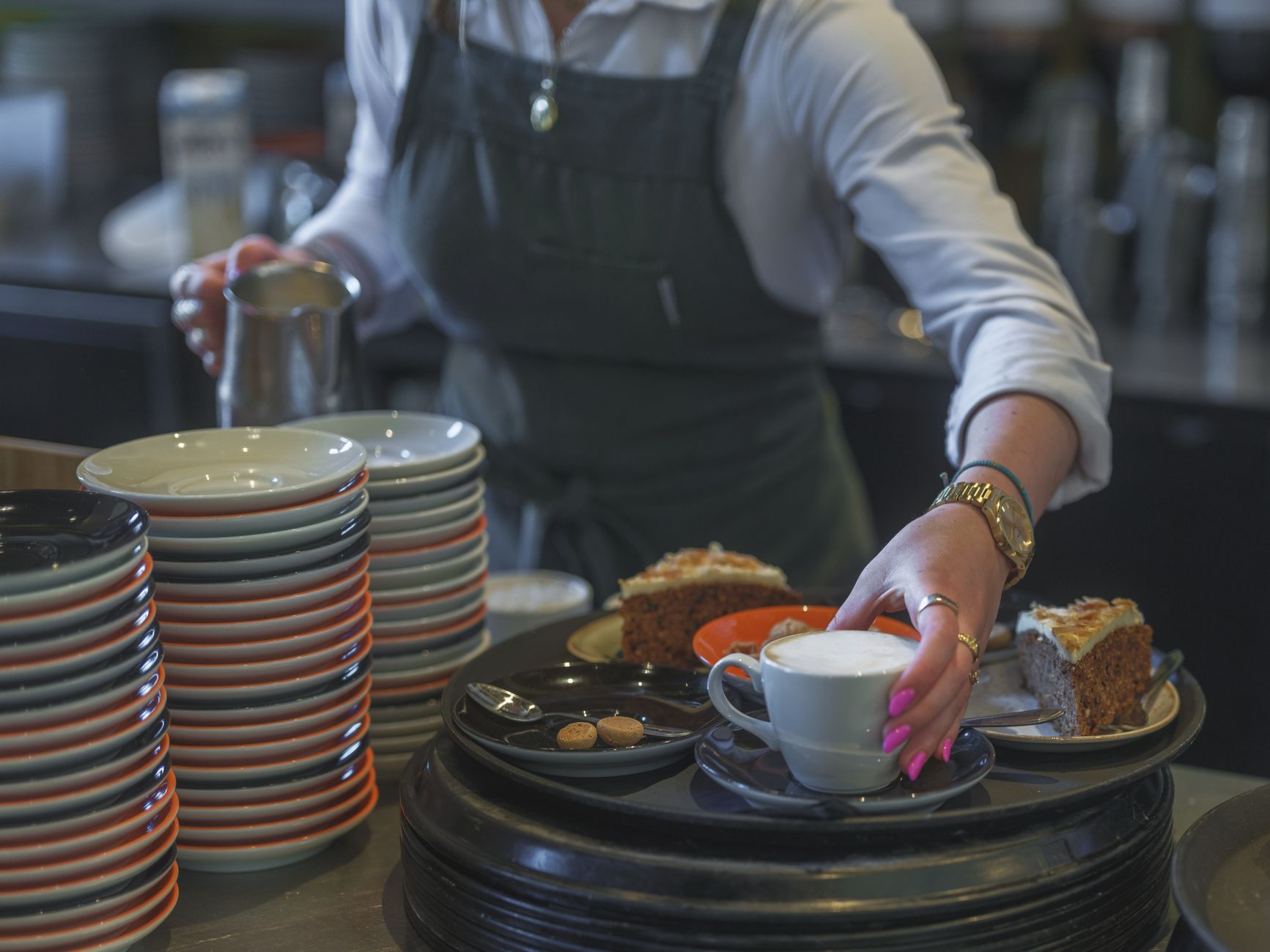 A café worker sets down a coffee and a slice of cake for a guest during a busy service.
