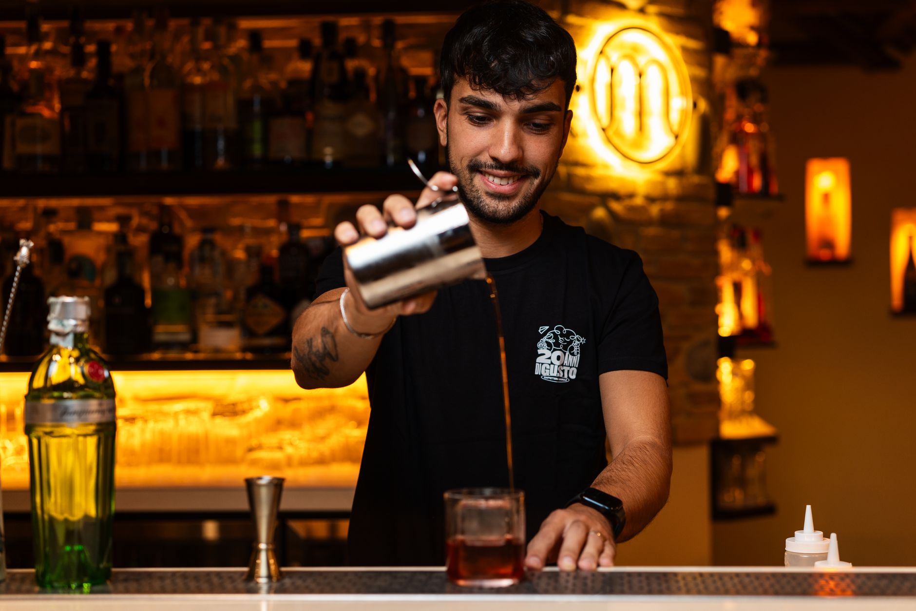 A bartender shakes a cocktail behind a lit bar.