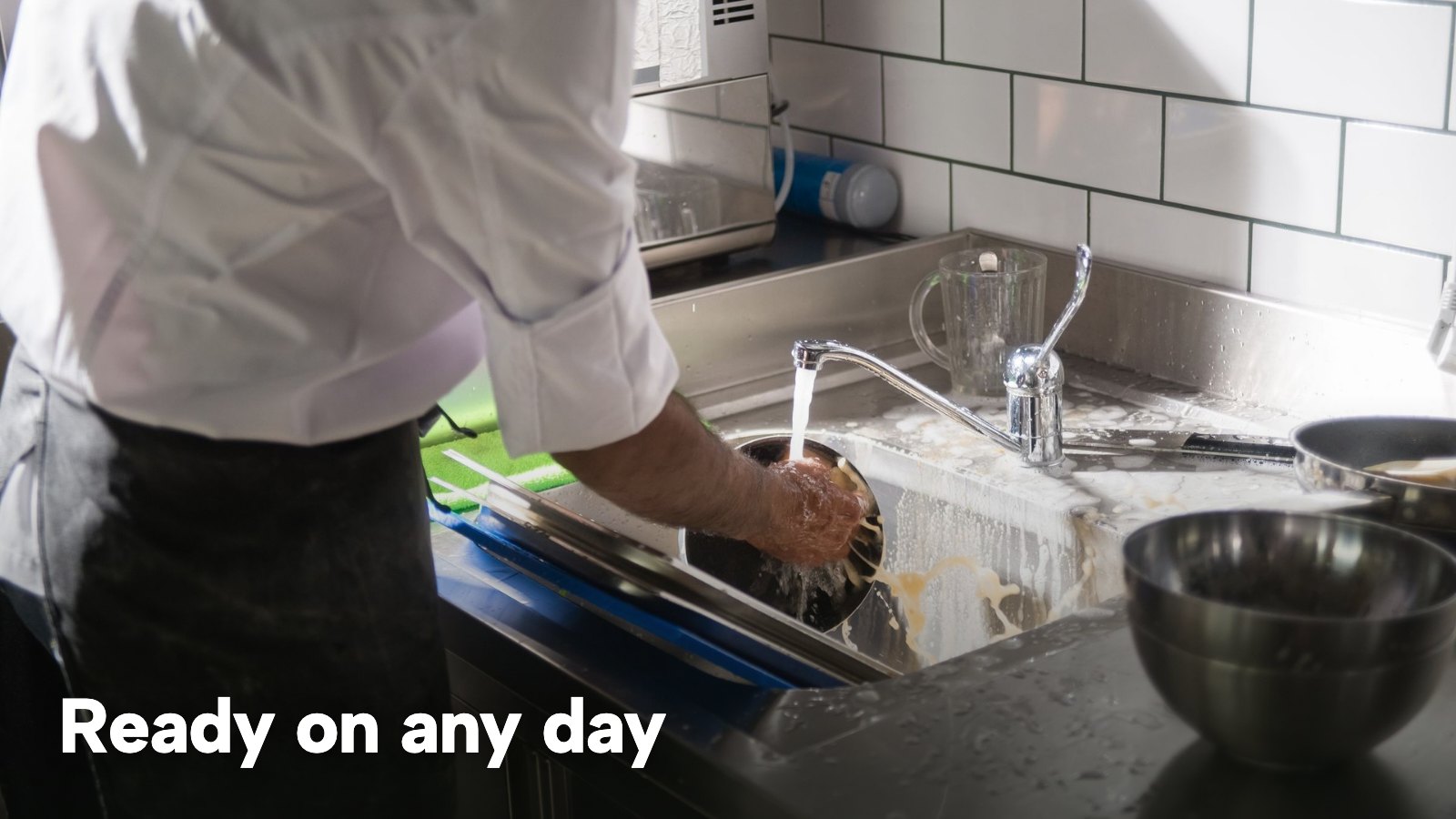 A cook washing equipment at a stainless steel sink in a commercial kitchen. The image carries the words "Ready on any day".
