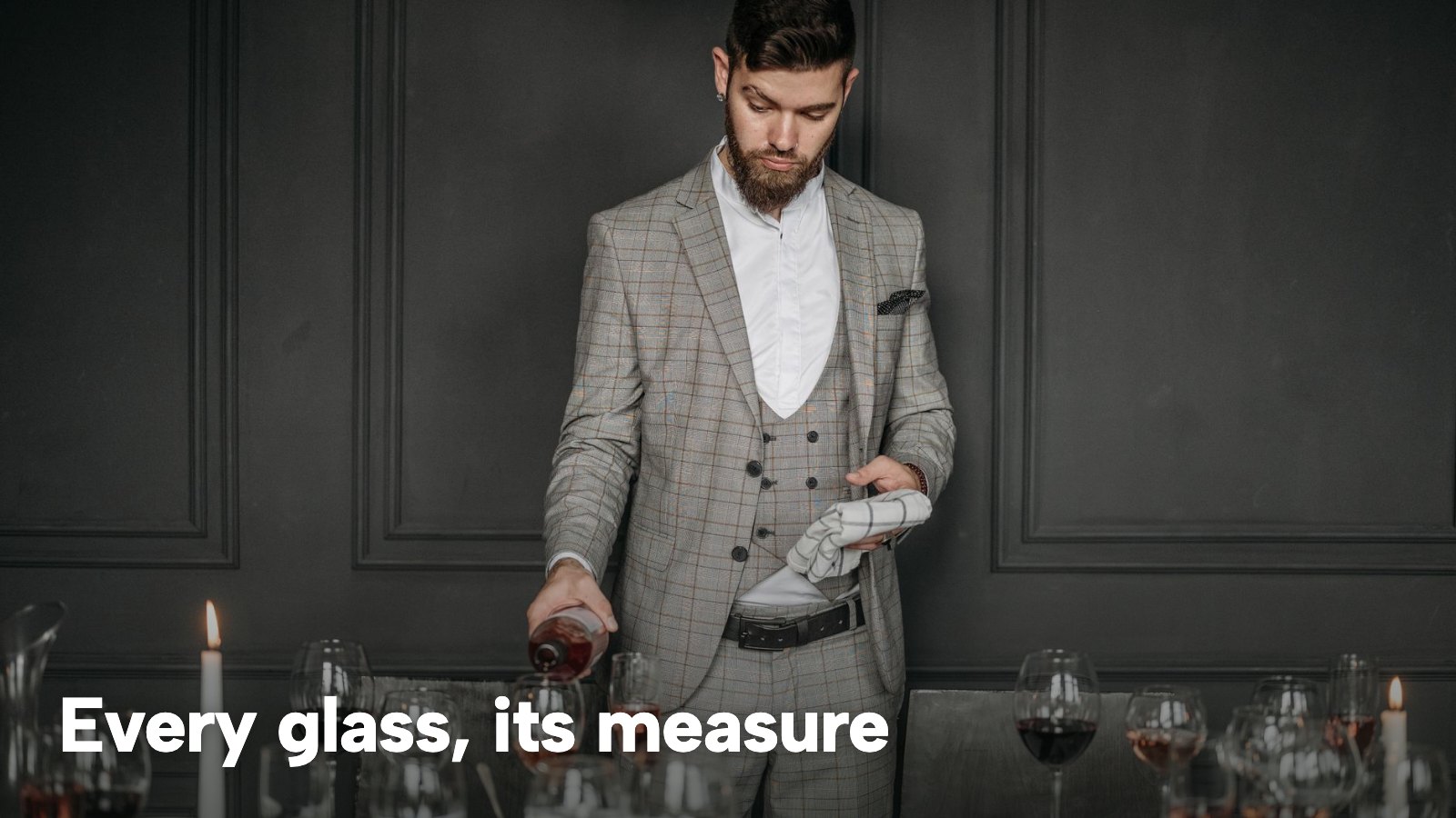 A sommelier pouring red wine into glasses at a candlelit dinner table. The image carries the words "Every glass, its measure".