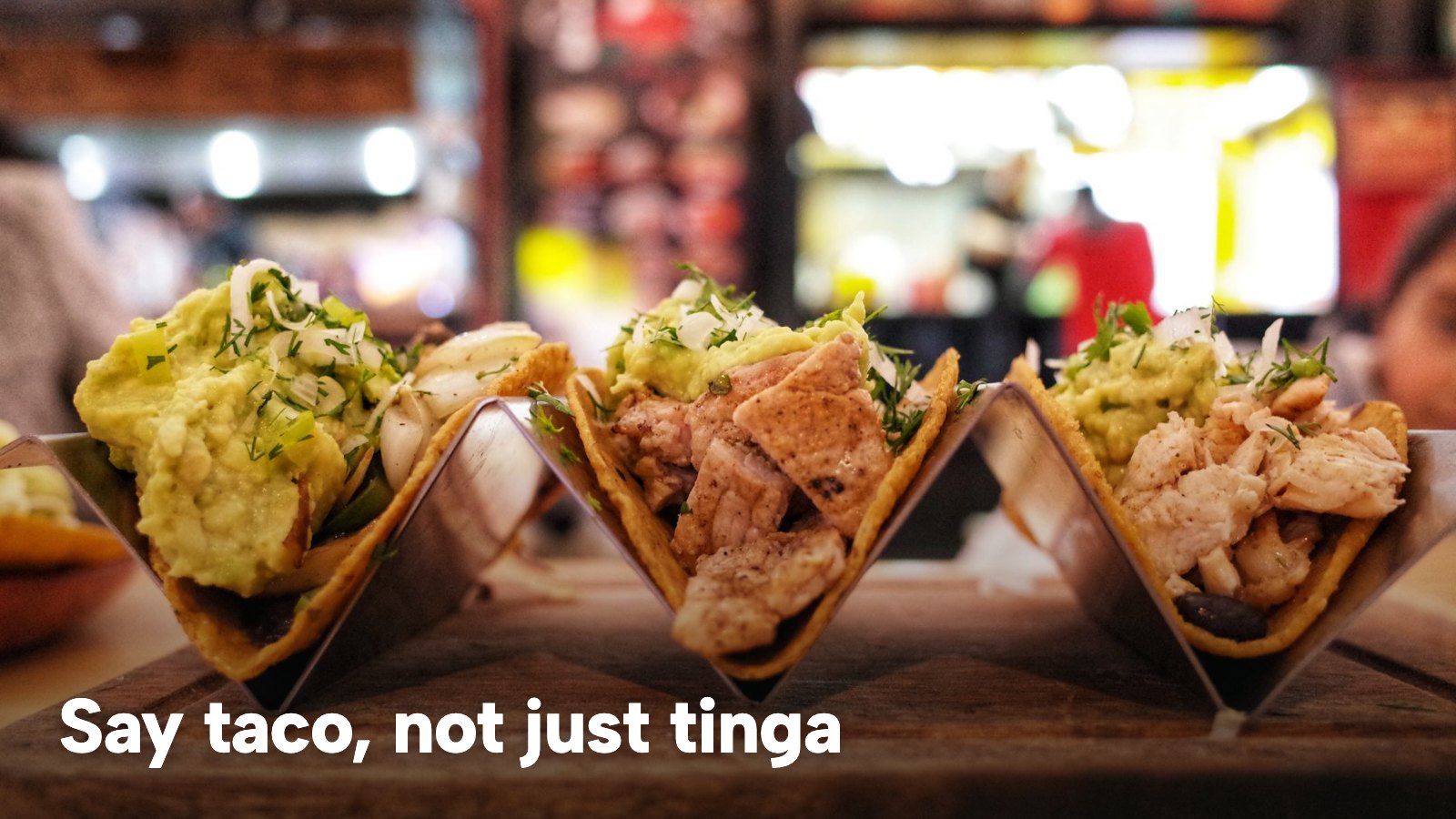 Three chicken tacos with guacamole, herbs and onions served in a restaurant. The image carries the words "Say taco, not just tinga".