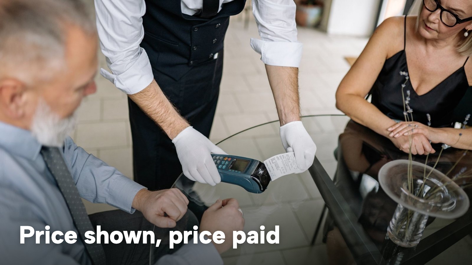 A waiter's gloved hands holding a card terminal and a printed receipt at a restaurant table. The image carries the words "Price shown, price paid".