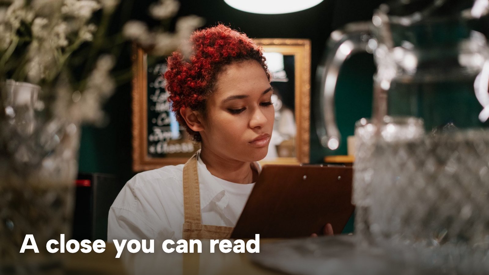 A server in an apron reading a clipboard behind the bar. The image carries the words "A close you can read".