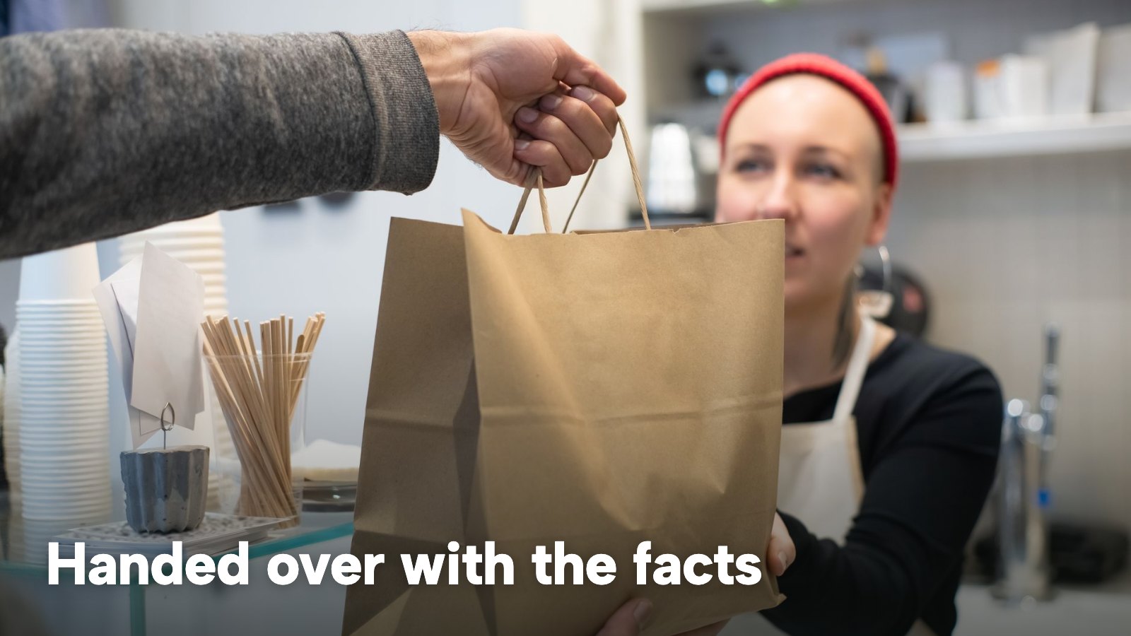 A paper takeaway bag is handed across a counter to a woman in a red beanie. The image carries the words "Handed over with the facts".
