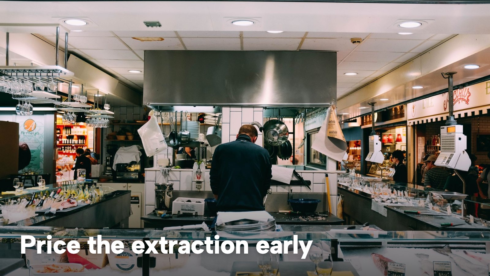 A chef working under a stainless steel extraction canopy in an open kitchen. The image carries the words "Price the extraction early".