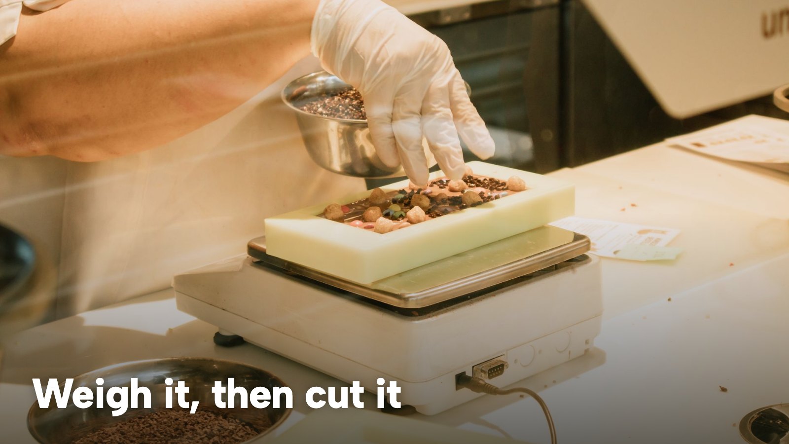 A gloved hand weighing food on a small kitchen scale. The image carries the words "Weigh it, then cut it".