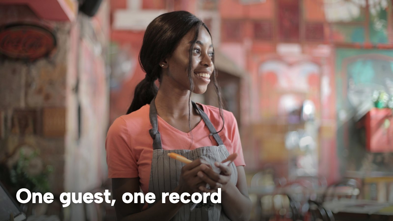 A smiling waitress in an apron writing on a notepad in a restaurant. The image carries the words "One guest, one record".