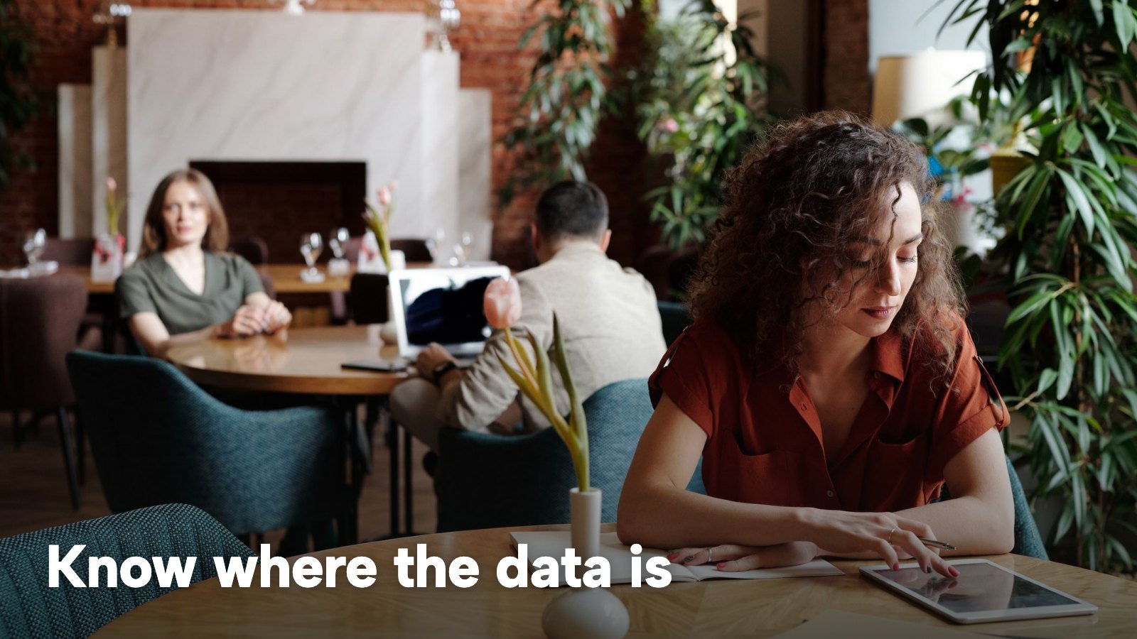 A woman at a restaurant table working on a tablet. The image carries the words "Know where the data is".