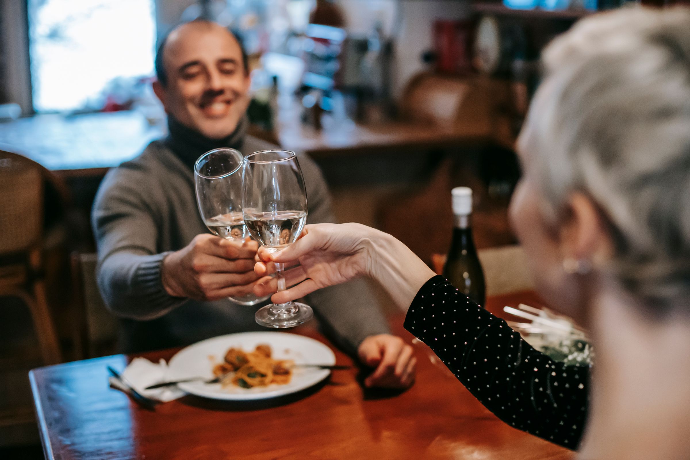 Two diners raising glasses of wine over dinner.