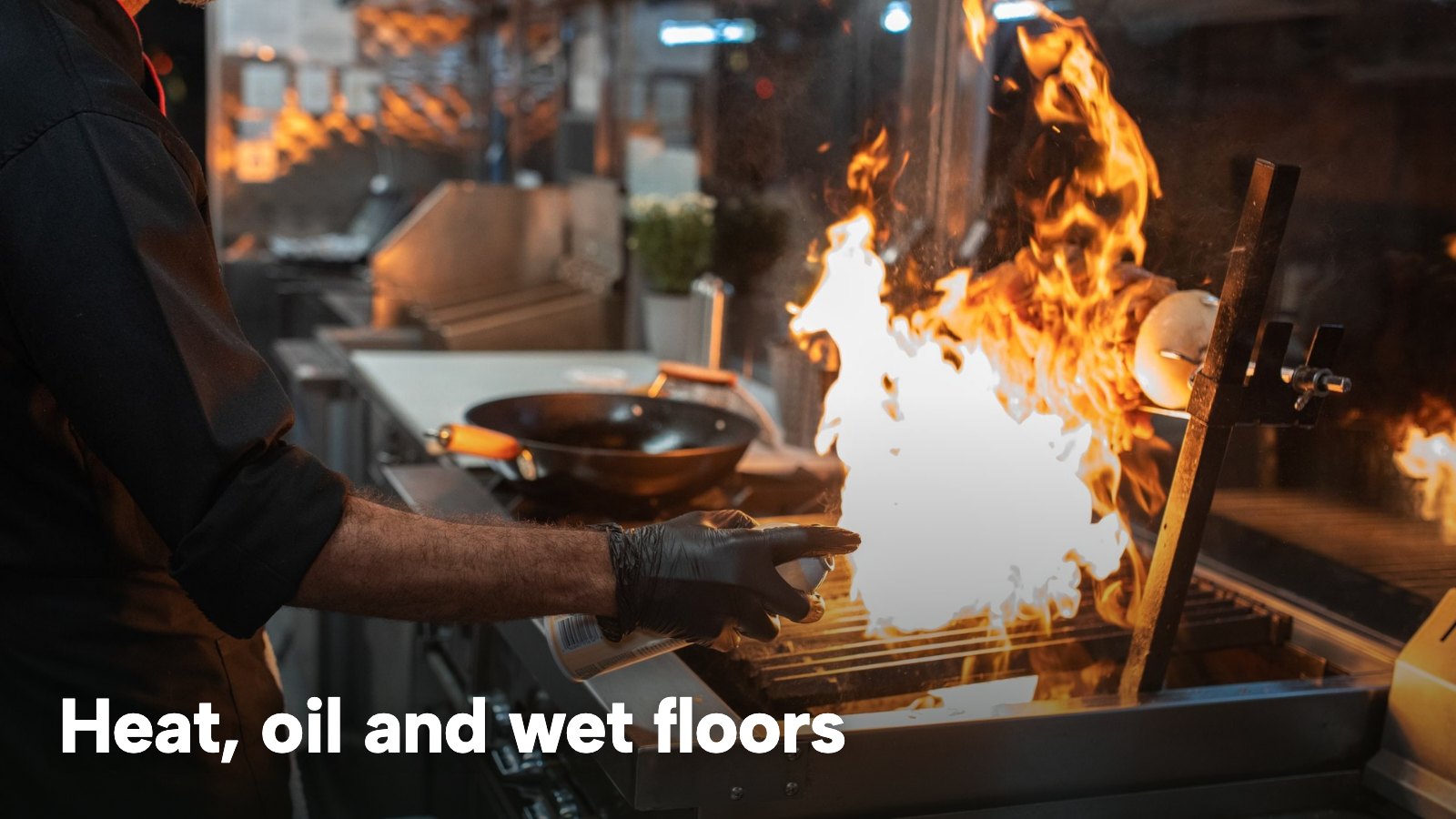 A chef grilling meat over an open flame in a professional kitchen. The image carries the words "Heat, oil and wet floors".