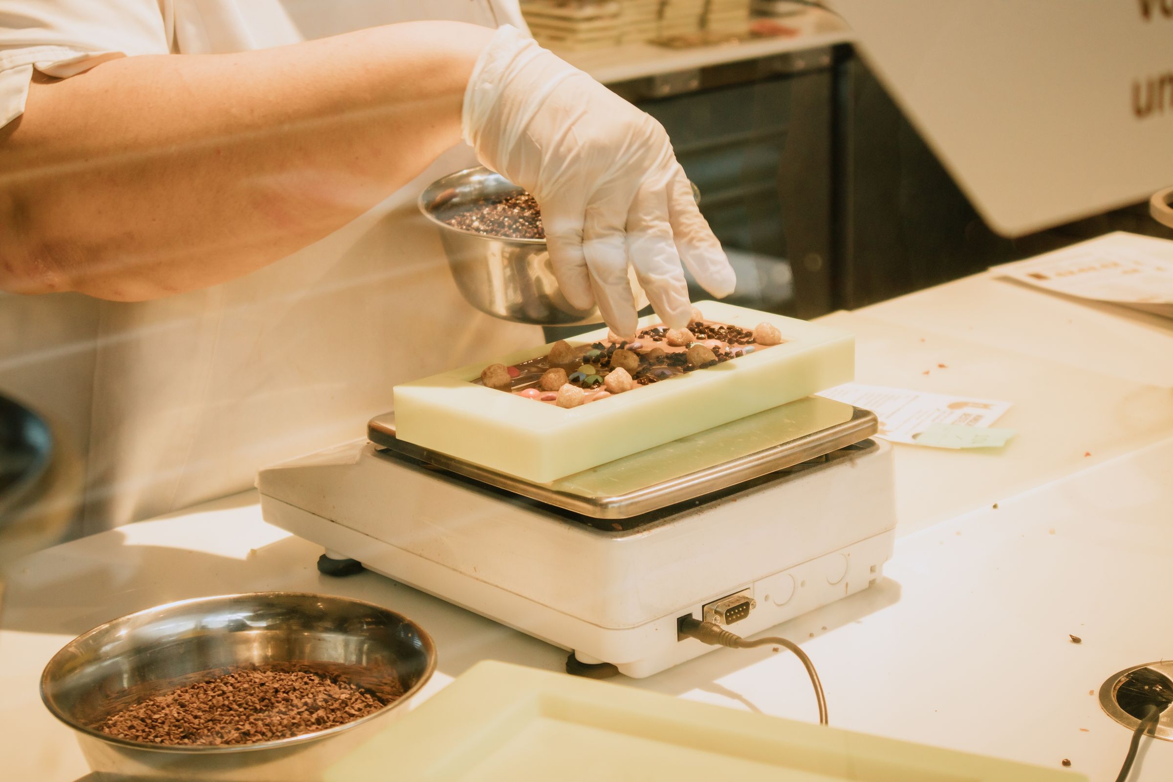 A gloved hand weighing an ingredient on a kitchen scale.