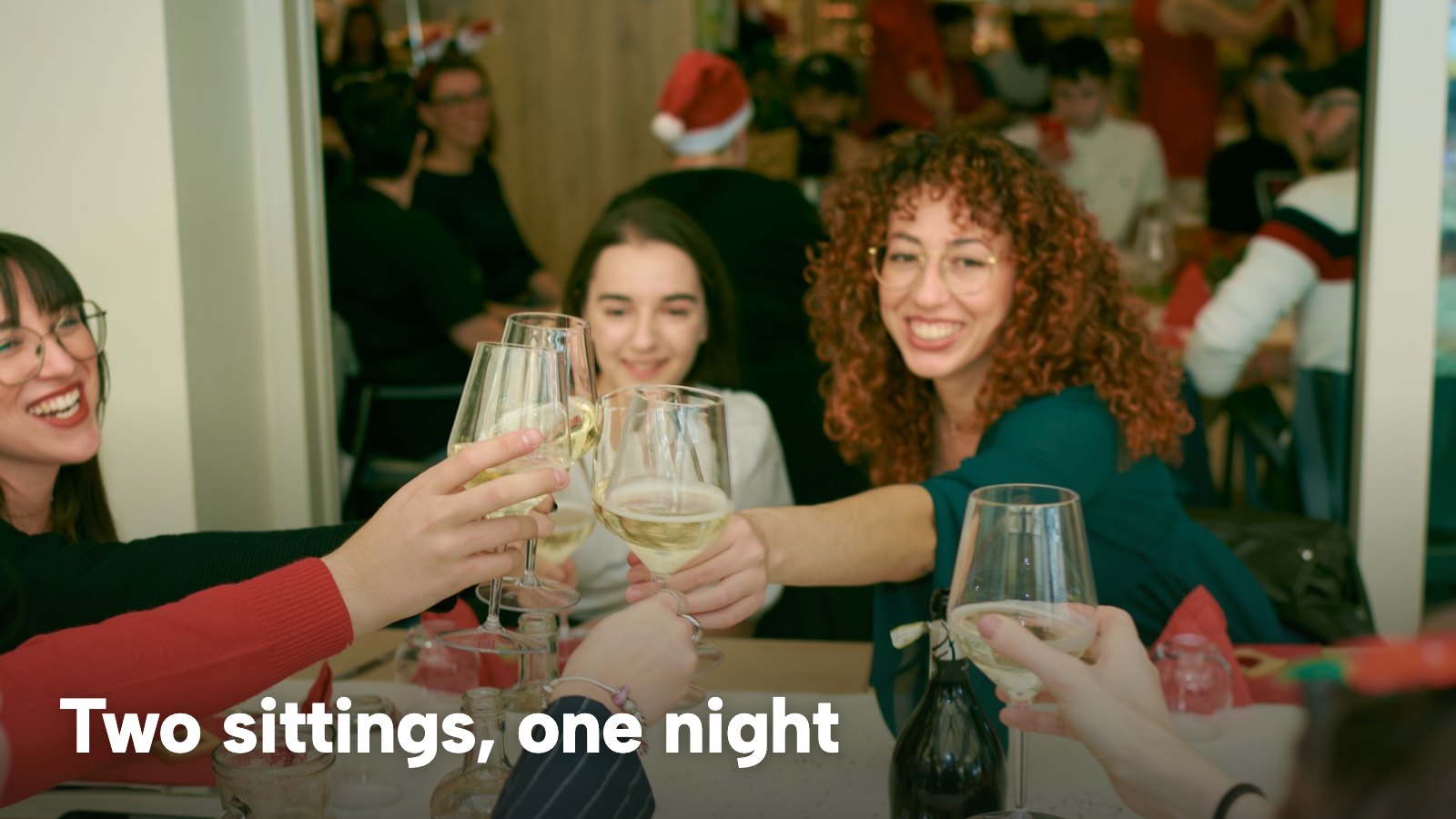 Friends toasting with wine glasses at a festive dinner table. The image carries the words "Two sittings, one night".