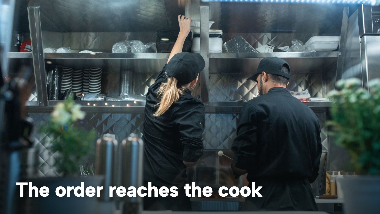 Two cooks in black working at the shelves of a restaurant kitchen. The image carries the words "The order reaches the cook".