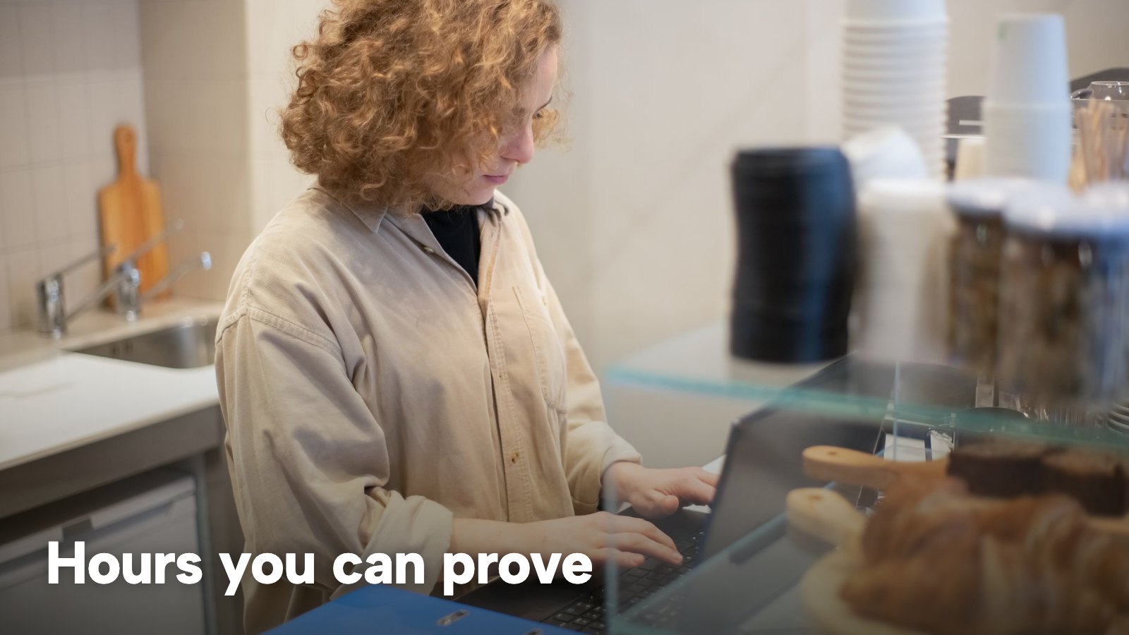 A woman works on a laptop behind a café counter. The image carries the words "Hours you can prove".