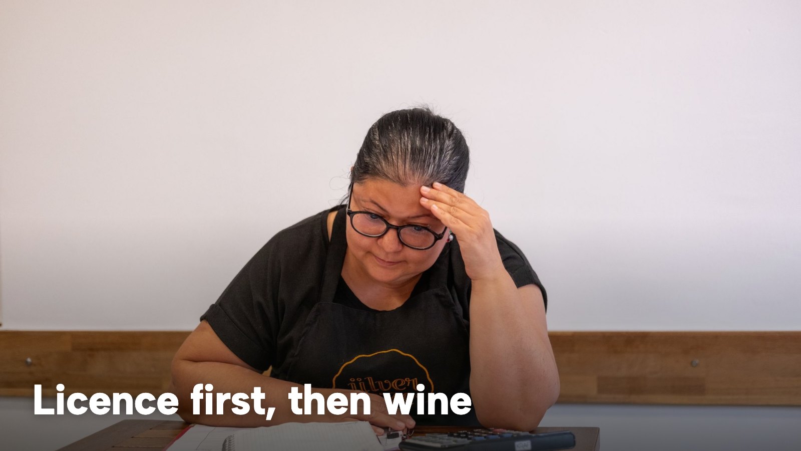 An owner at a desk working through paperwork with a calculator. The image carries the words "Licence first, then wine".