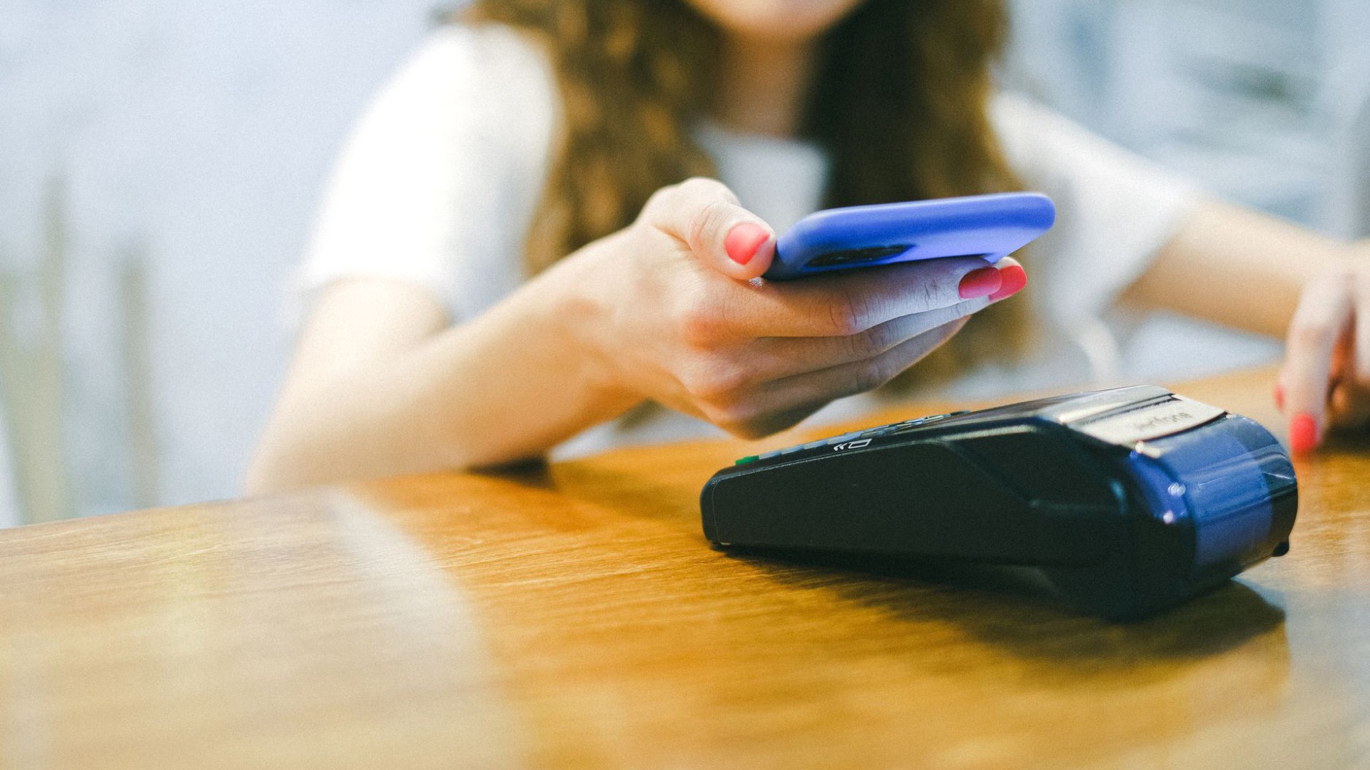 A guest taps a phone on a card terminal resting on a wooden table.