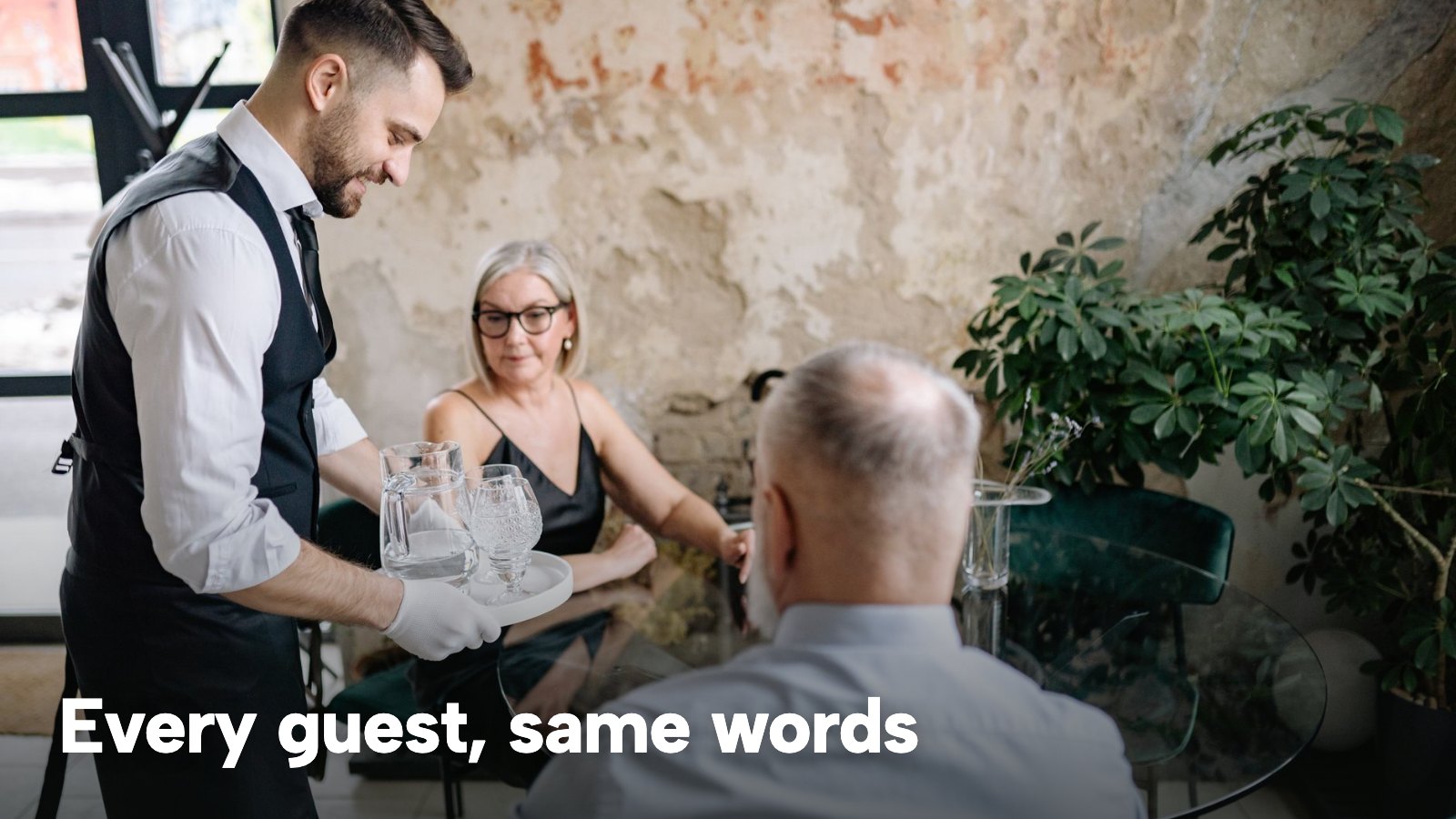 A waiter serving two guests at a table in a restaurant with plants. The image carries the words "Every guest, same words".