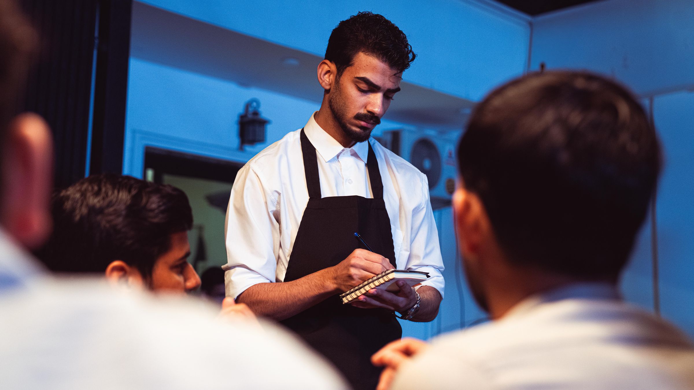 A server taking notes while talking with two colleagues in a restaurant.