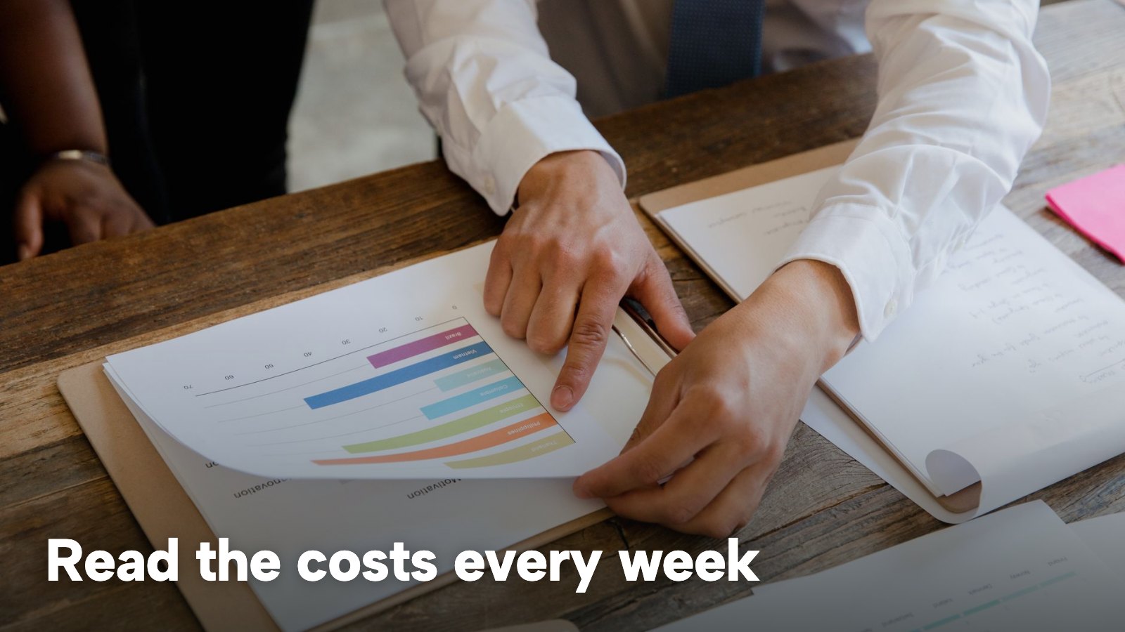 Hands pointing at printed bar charts on a desk. The image carries the words "Read the costs every week".