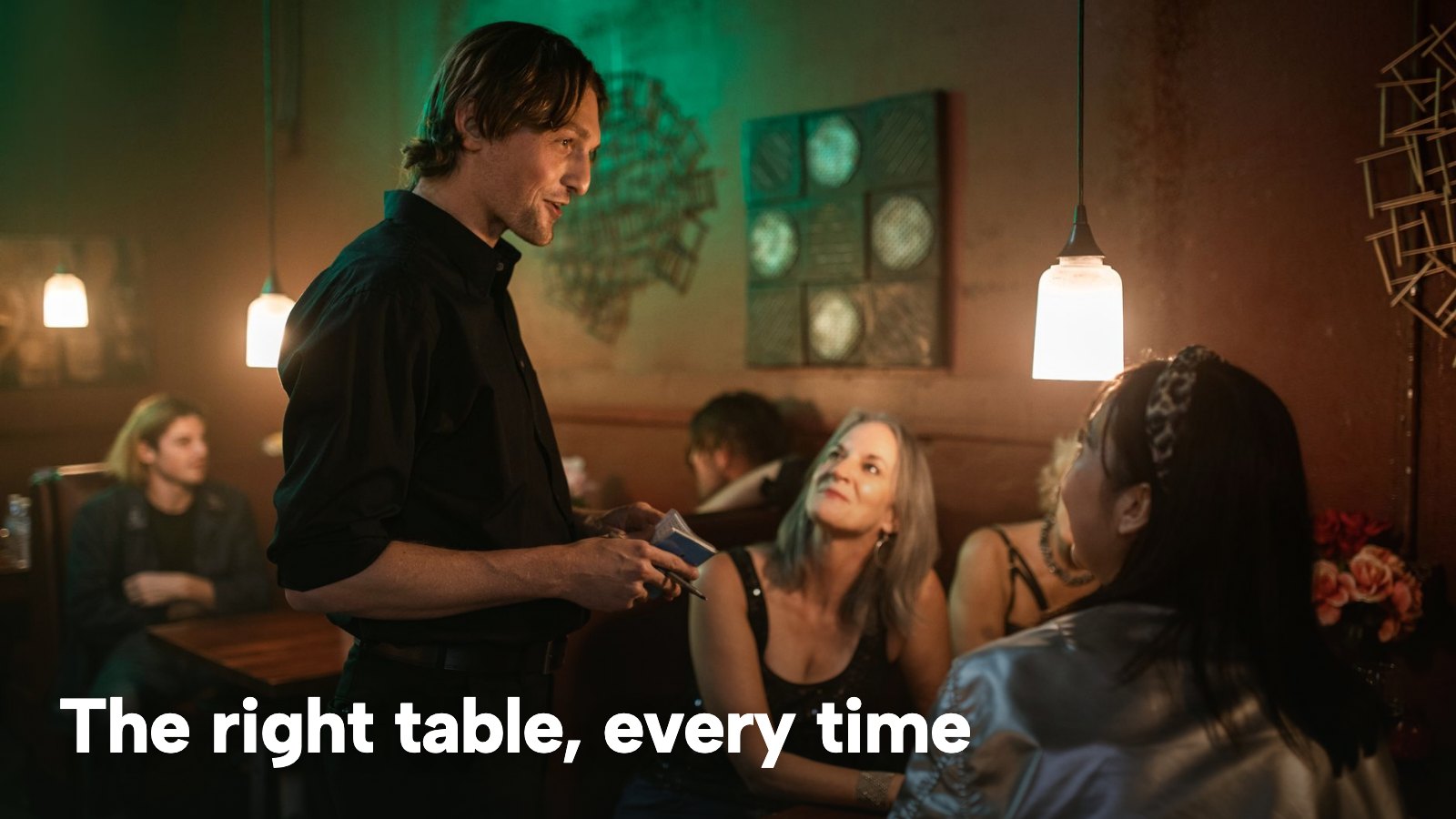 A server takes an order from a table of guests in a warmly lit restaurant. The image carries the words "The right table, every time".