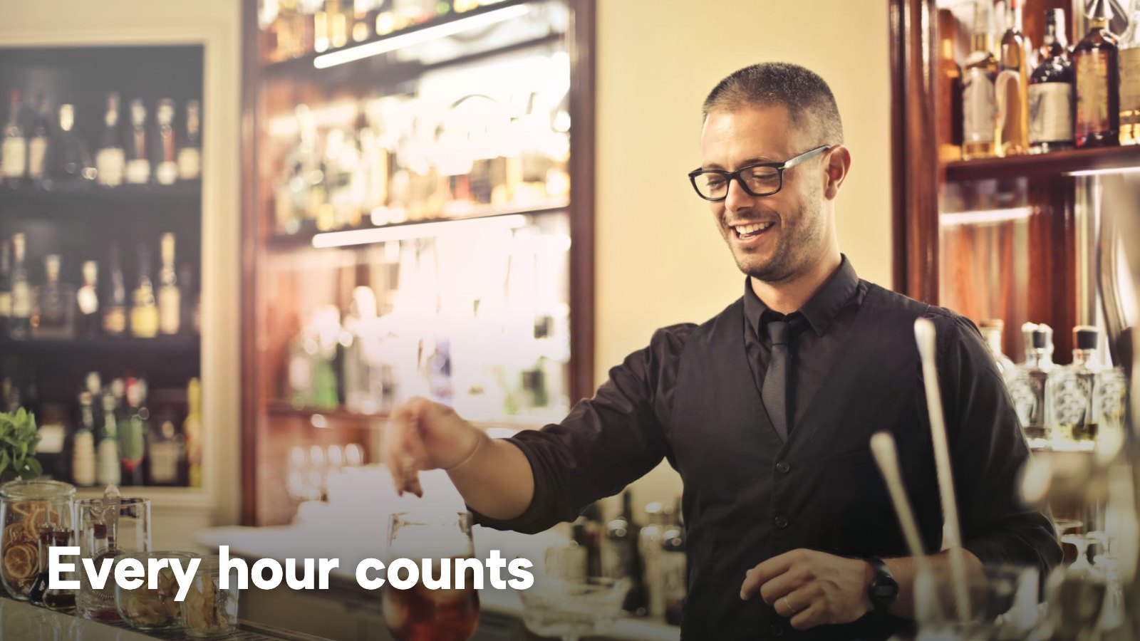 A smiling bartender serves a drink across the bar. The image carries the words "Every hour counts".