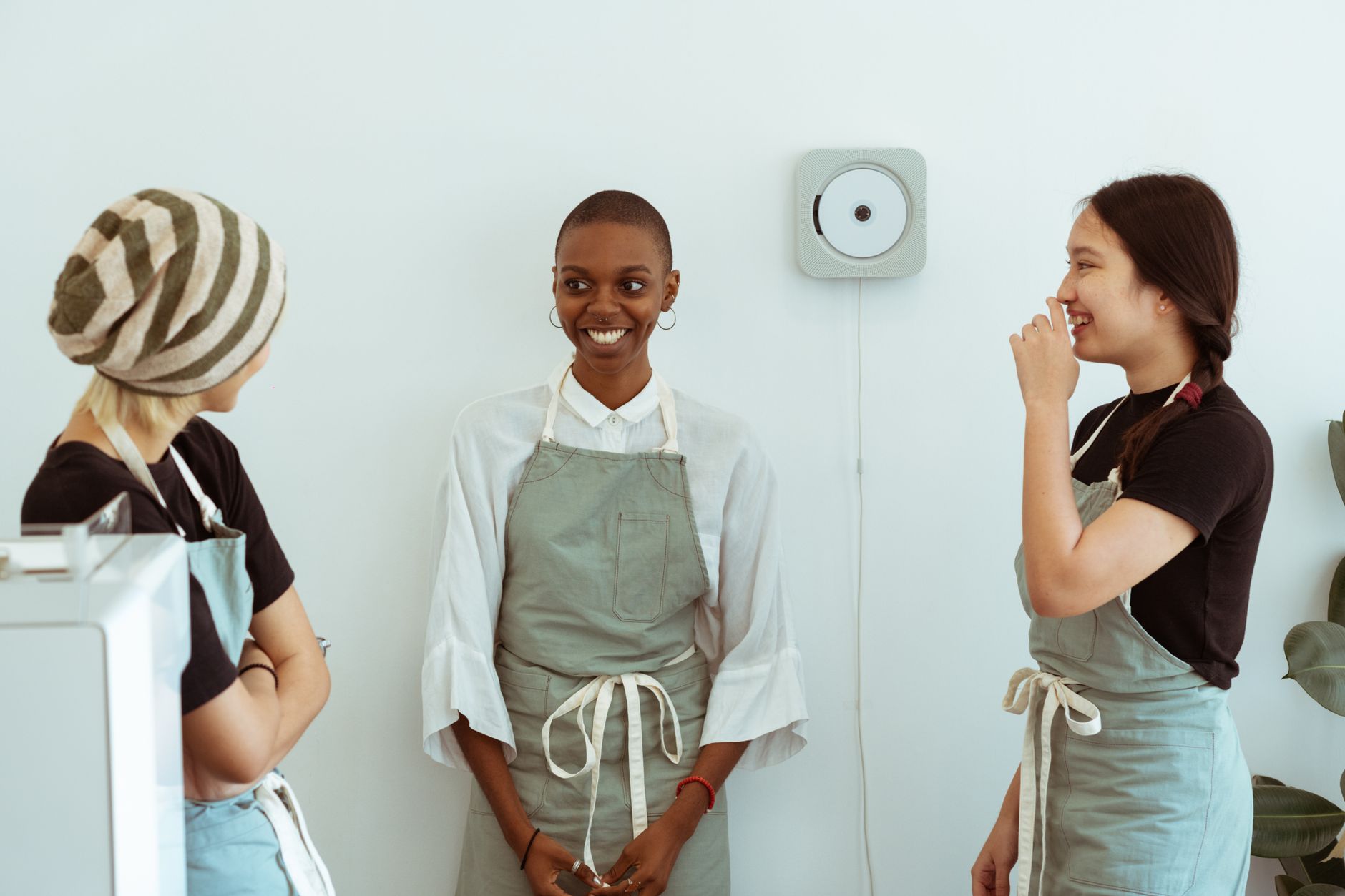 Three young café staff in aprons talk together beside the counter.