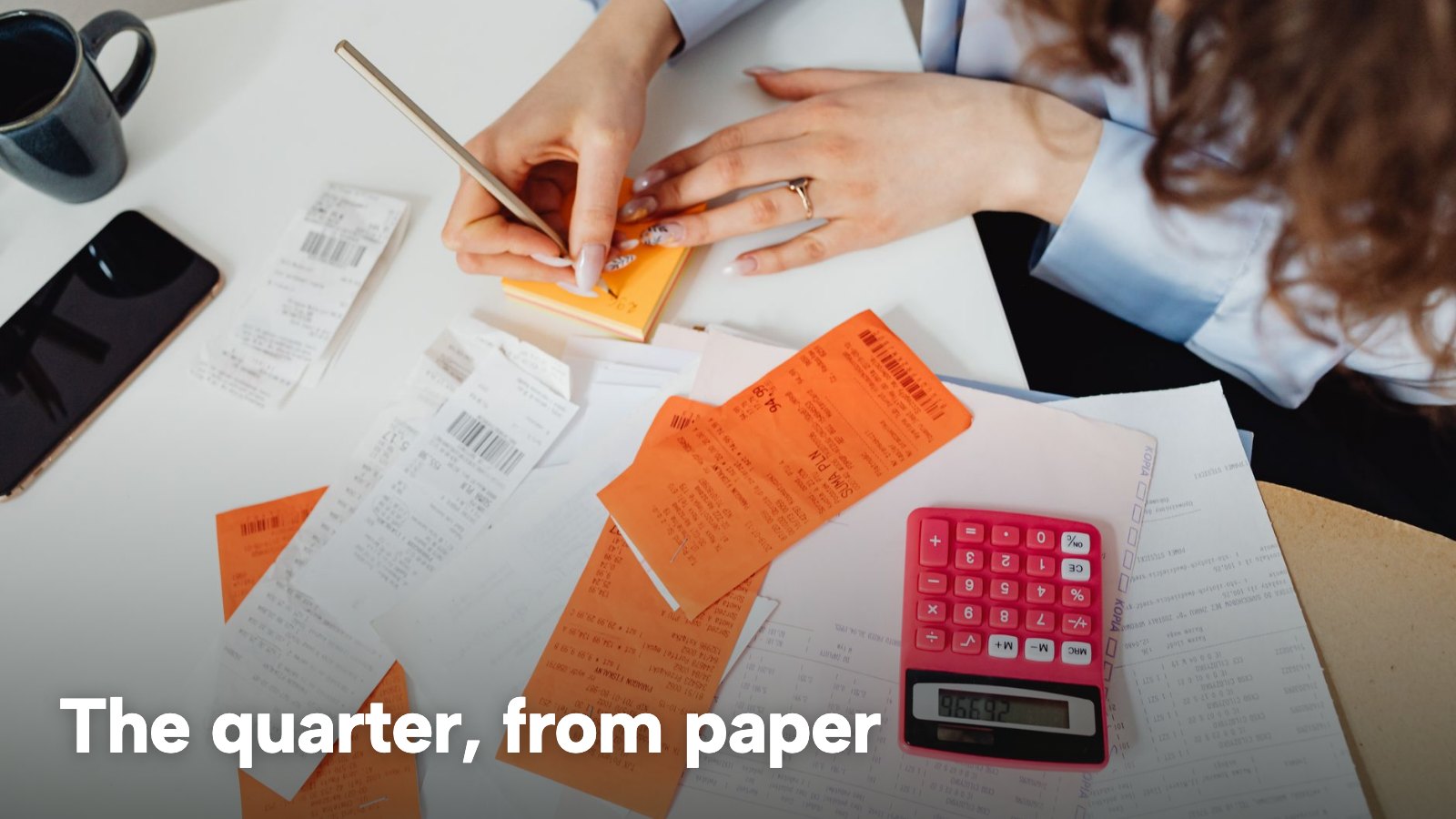 A person sorts receipts beside a pink calculator on a desk. The image carries the words "The quarter, from paper".