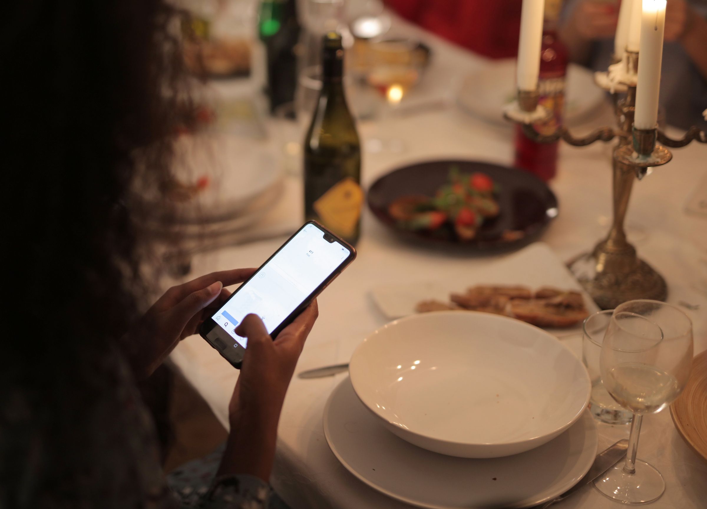 A diner holding a smartphone at a candlelit restaurant table.