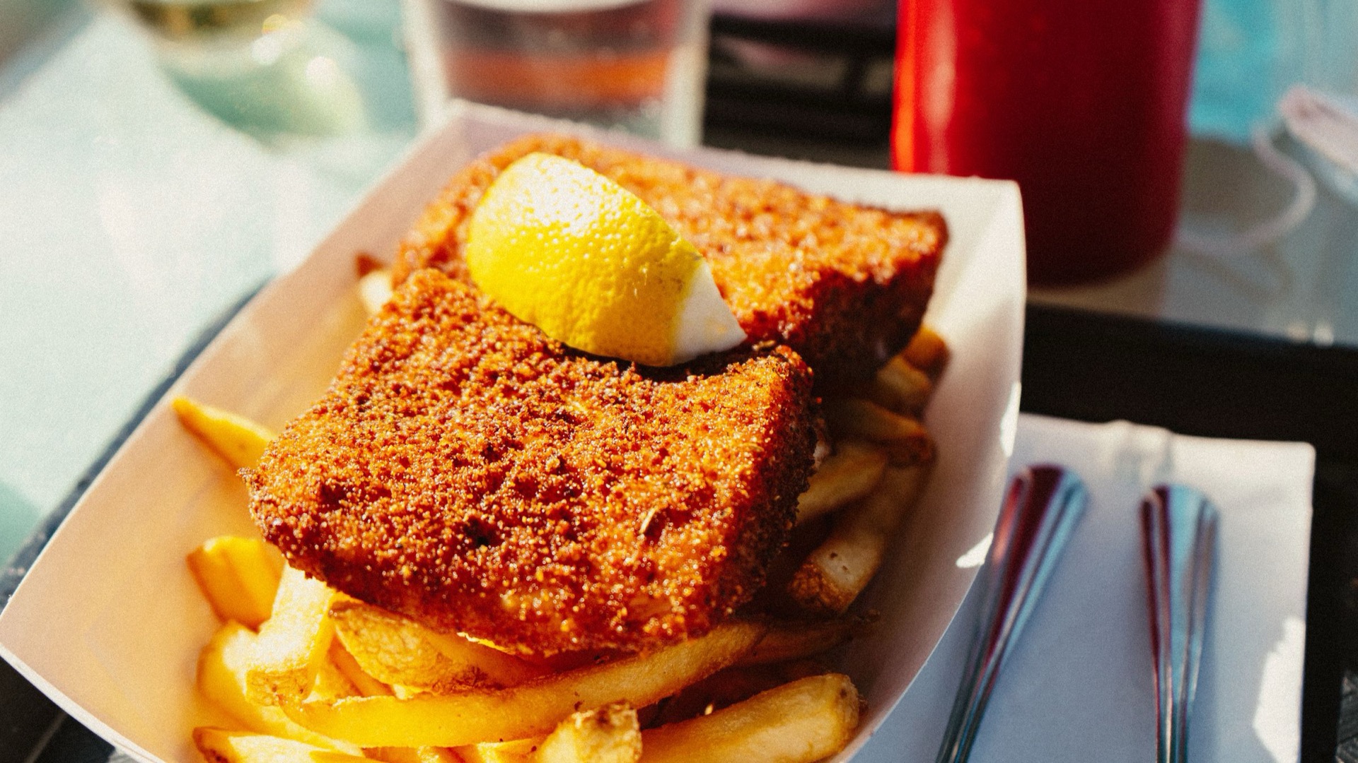 Fish and chips with a lemon wedge in a paper tray.