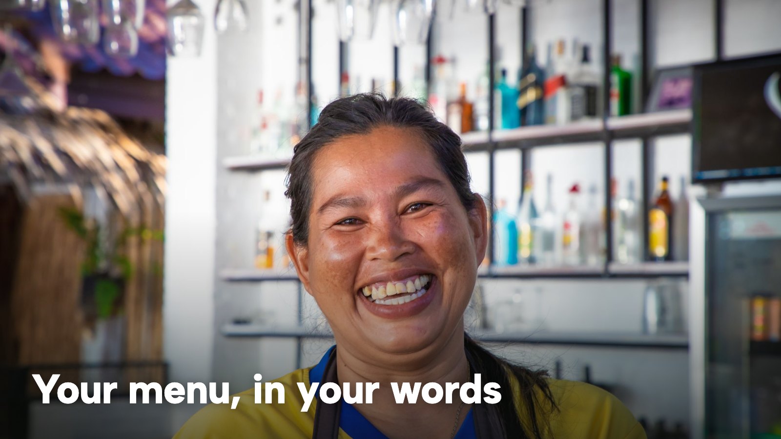 A smiling Thai restaurant owner standing at a bar counter. The image carries the words "Your menu, in your words".