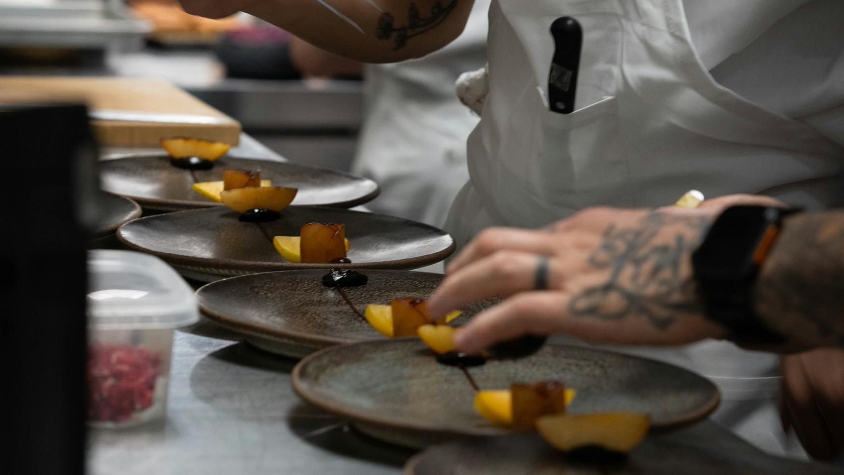 A chef plating several dishes in a professional restaurant kitchen.