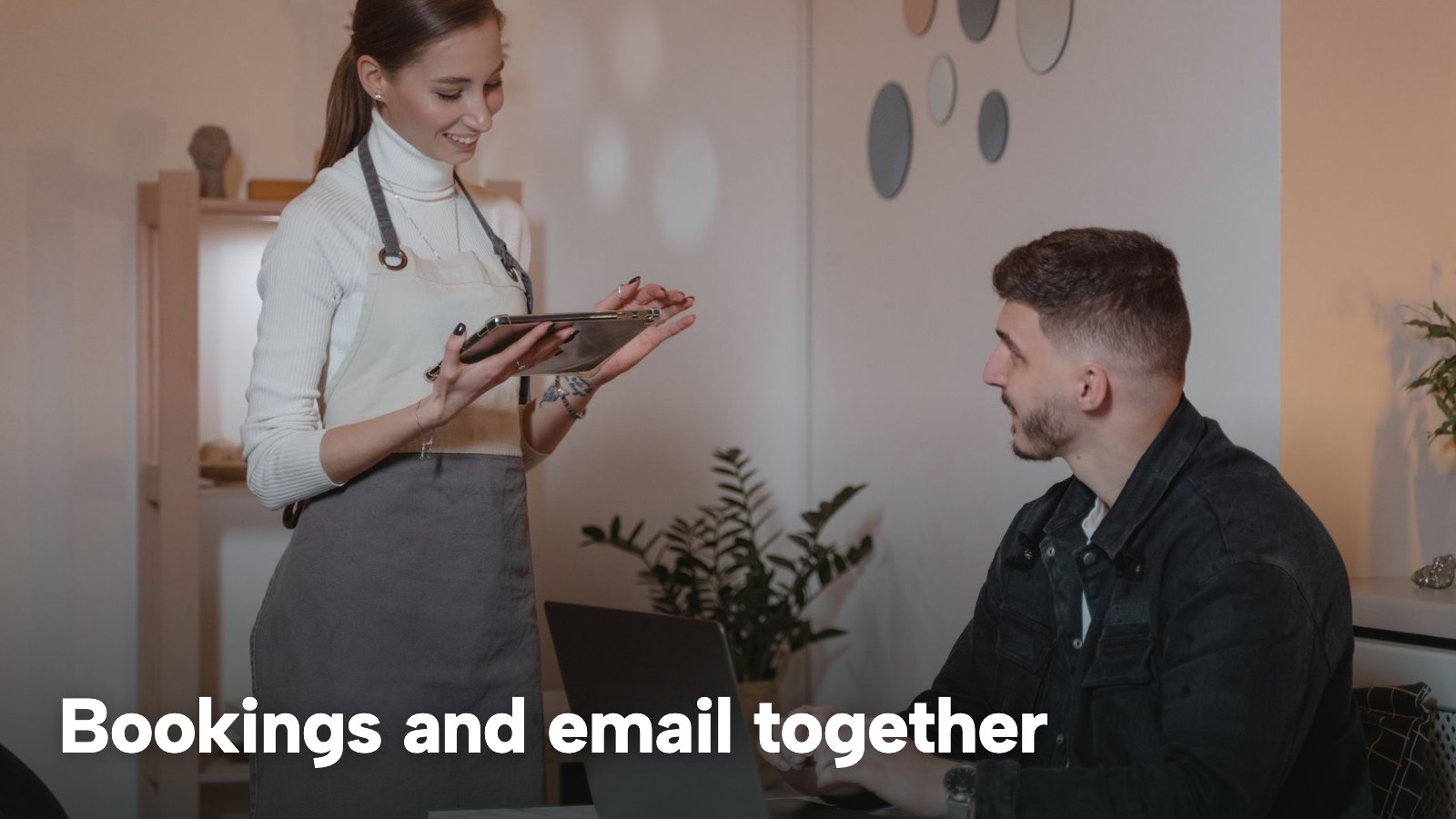 A waitress holding a tablet beside a seated man working on a laptop. The image carries the words "Bookings and email together".
